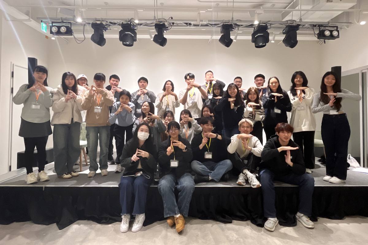近三十位 BT 幹部在舞台上的大合照，每個人用手比出同一個手勢